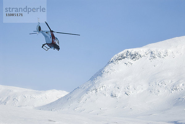 Ein Hubschrauber fliegt über schneebedeckte Berge  Schweden.
