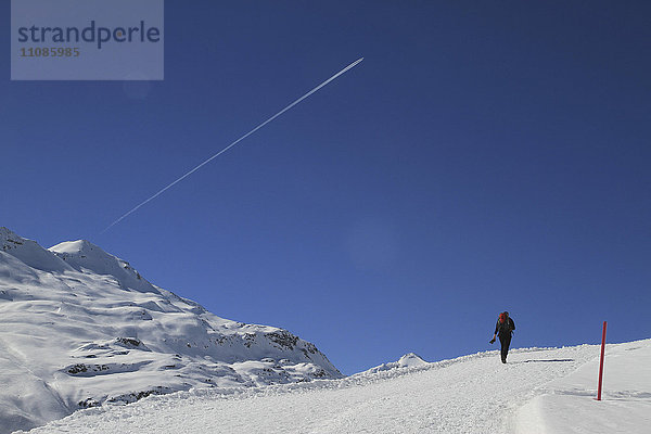 Rückansicht der Person  die auf einem schneebedeckten Berg gegen den blauen Himmel wandert.