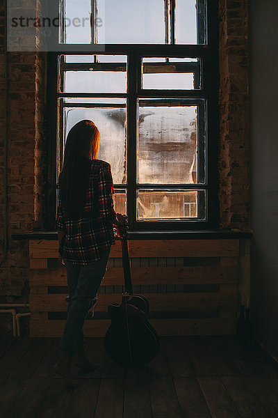 Durchgehende Rückansicht der Frau mit Gitarre am Fenster zu Hause