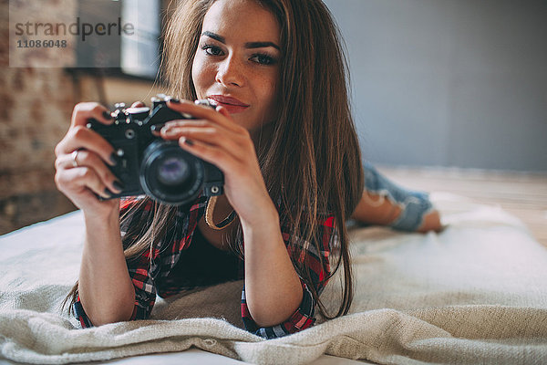 Porträt einer jungen Frau mit Spiegelreflexkamera im Bett zu Hause