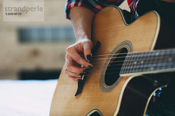 Beschnittenes Bild einer Frau  die zu Hause Gitarre spielt.