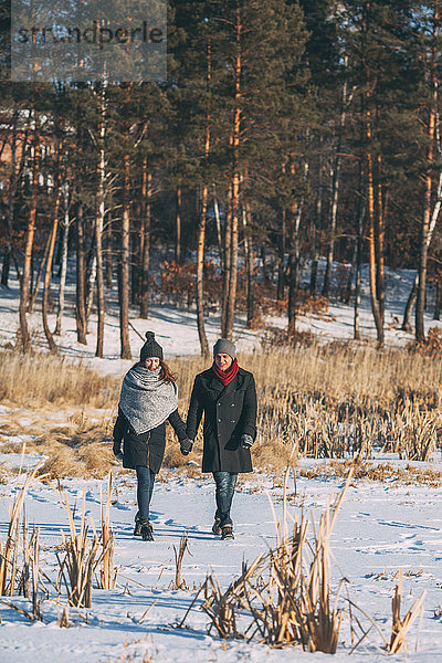 Junges Paar hält sich beim Spaziergang auf schneebedecktem Feld an den Händen