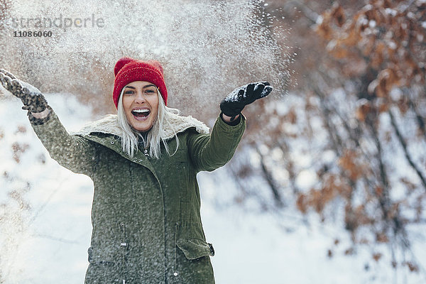 Porträt einer fröhlichen jungen Frau beim Spielen im Schnee