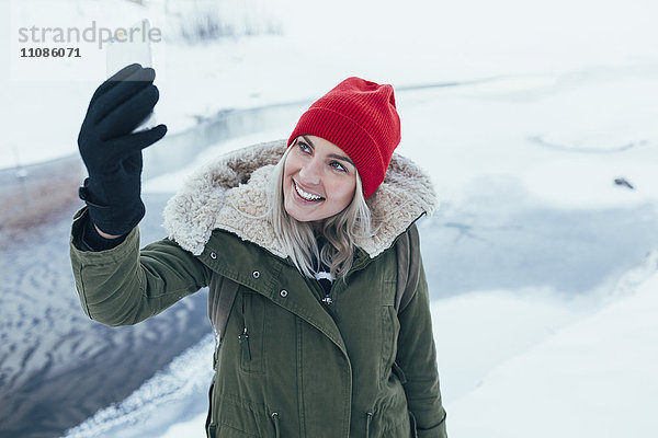 Glückliche junge Frau nimmt Selfie auf Smartphone im Winter