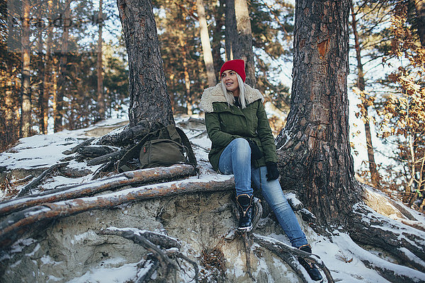 Volle Länge der jungen Frau  die im verschneiten Wald sitzt