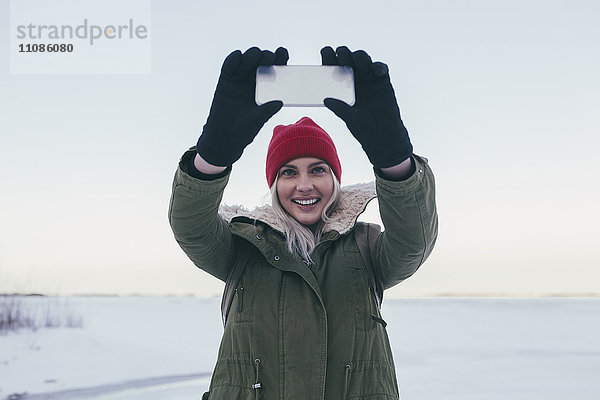 Junge Frau nimmt Selfie auf Smartphone im Winter