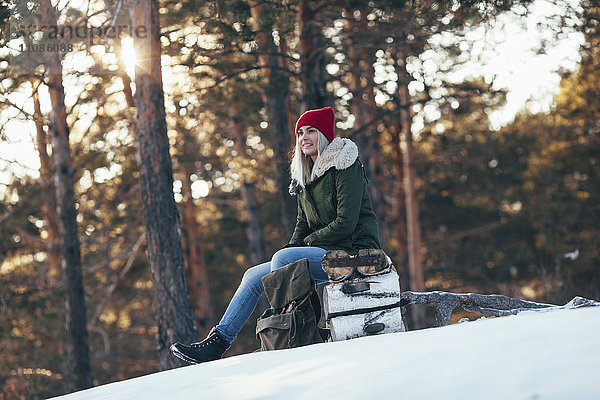 Frau schaut weg  während sie im Winter auf dem Baumstamm sitzt.