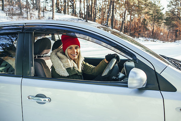 Porträt einer lächelnden Frau in warmer Kleidung beim Autofahren
