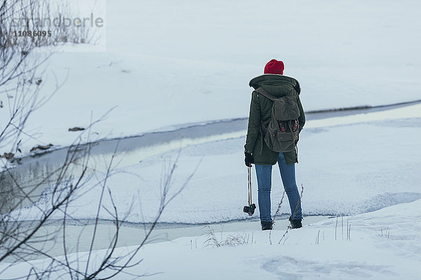 Frau mit Rucksack  die die Kamera hält  während sie im Winter auf dem Feld steht.