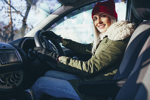 Porträt einer glücklichen jungen Frau in warmer Kleidung beim Autofahren