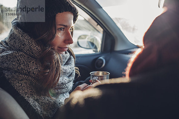 Junge Frau mit Kaffeetasse und Blick auf den Mann im Auto