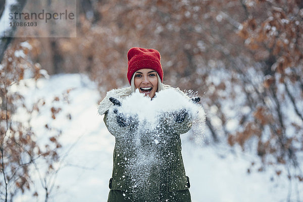 Porträt einer glücklichen jungen Frau beim Spielen mit Schnee