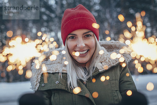 Porträt einer lächelnden Frau  die im Winter Wunderkerzen hält.