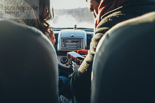 Beschnittenes Bild des Paares mit Smartphone im Auto