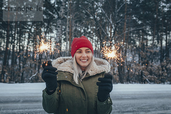 Lächelnde Frau hält im Winter Wunderkerzen.