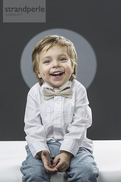 Porträt eines fröhlichen Jungen mit Fliege auf grauem Hintergrund