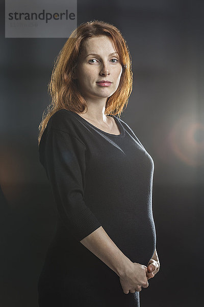 Porträt einer schwangeren Frau  die den Bauch vor grauem Hintergrund berührt.