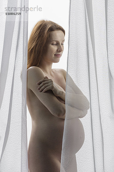 Nackte  schwangere Frau  die vor einem weißen Hintergrund steht.