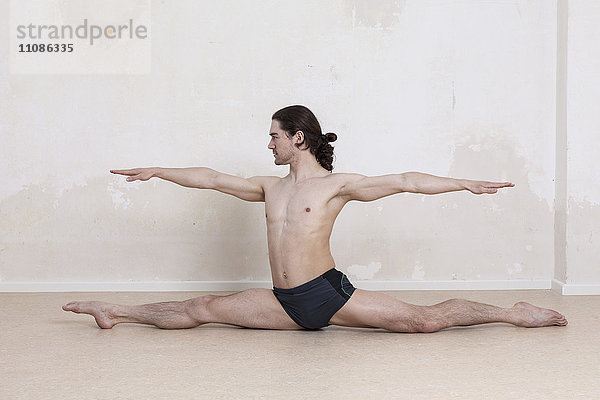 Selbstbewusster Mann mit ausgestreckten Armen  der beim Yoga Spagat macht.