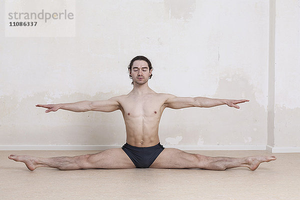 Mann mit ausgestreckten Armen bei der Durchführung von Yoga vor weißem Hintergrund