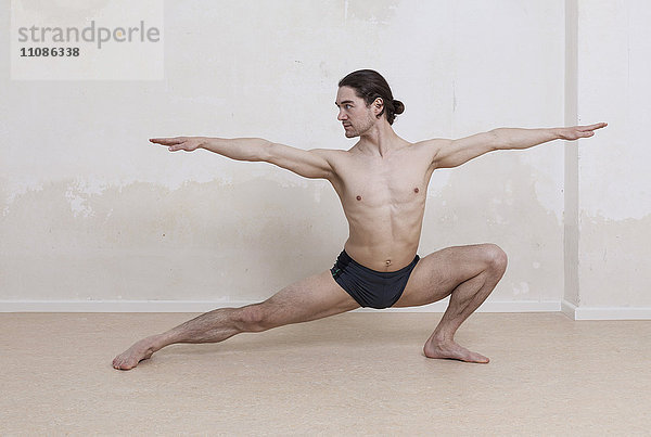 Entschlossener Mann  der Yoga in Kriegerposition vor weißem Hintergrund praktiziert.