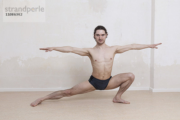 Porträt eines entschlossenen Mannes  der Yoga in Kriegerposition vor weißem Hintergrund praktiziert.