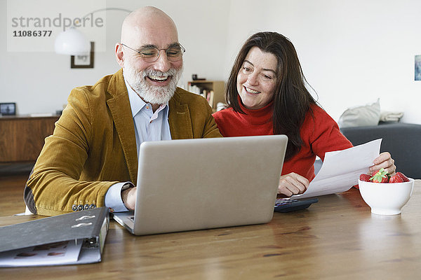Glückliches reifes Paar mit Laptop auf dem Tisch zu Hause
