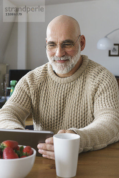 Erwachsener Mann mit digitalem Tablett auf dem Tisch zu Hause