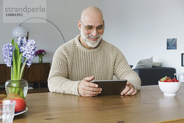 Lächelnder reifer Mann mit digitalem Tablett auf dem Tisch zu Hause