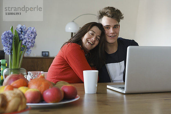 Glückliche Mutter und Sohn sitzend mit Laptop auf dem Tisch zu Hause