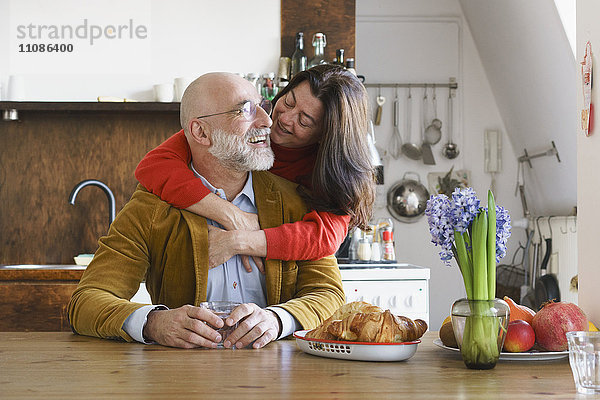 Ein glückliches Paar umarmt und lächelt am Tisch zu Hause.