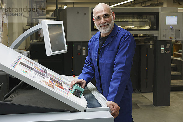 Porträt eines lächelnden  reifen Arbeiters  der an der Druckmaschine steht.