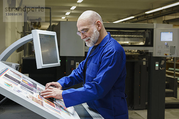 Ausgereifter Mann bei der Qualitätskontrolle des Ausdrucks mit Scanner an der Druckmaschine