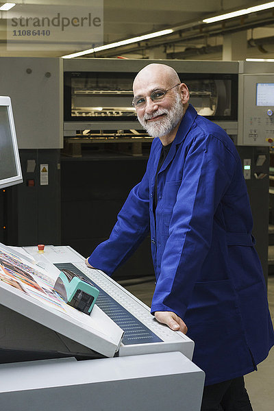 Porträt eines lächelnden  reifen Arbeiters  der an der Druckmaschine steht.