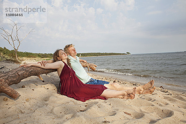 Freunde  die sich entspannen  während sie sich am Strand gegen den Himmel lehnen.