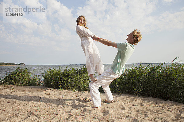 Frau balanciert auf dem Knie des Freundes am Strand gegen den Himmel