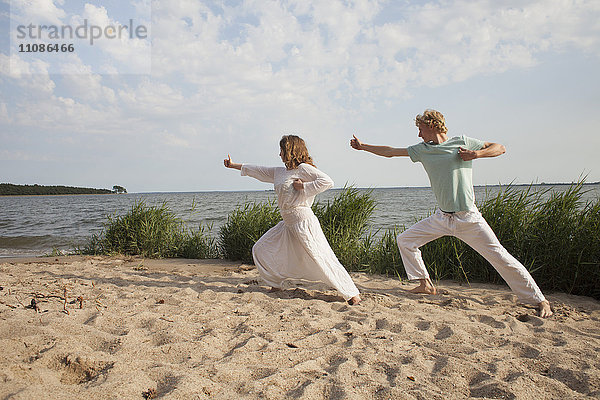 Freunde praktizieren Yoga am Meer am Strand gegen den Himmel