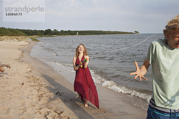 Frau spritzt Wasser auf Freund mit Spritzpistole am Strand