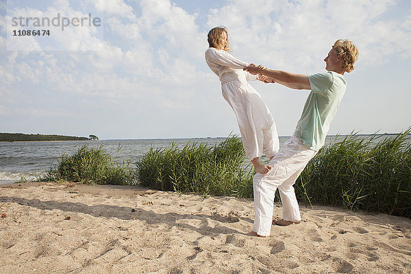 Freund balanciert auf dem Knie des Mannes am Strand gegen den Himmel.
