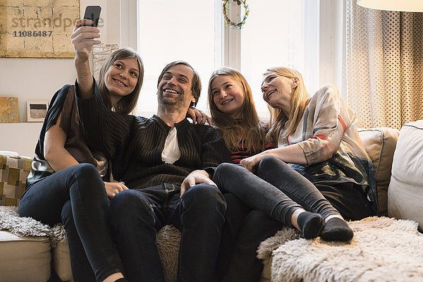 Glückliche vierköpfige Familie  die zu Hause über das Handy spricht