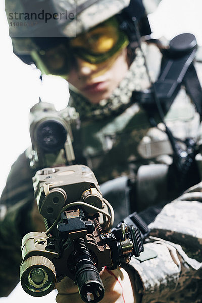 Soldatin  die vor weißem Hintergrund auf das Gewehr zielt.