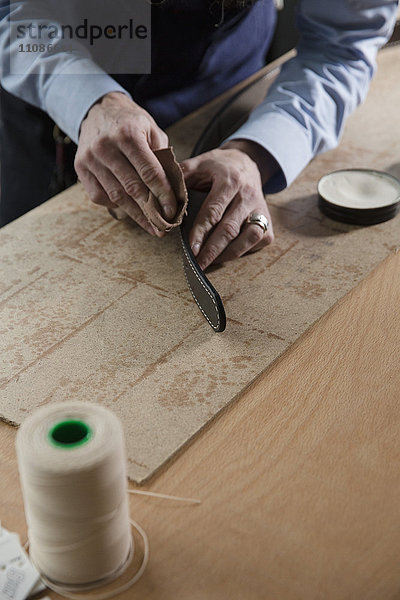 Hochwinkelansicht des Mannes  der den Ledergürtel auf dem Holztisch reibt.