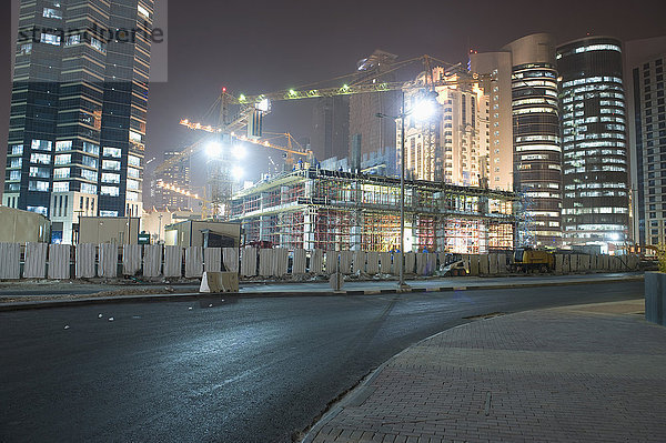 Straße gegen beleuchtete Baustelle und Gebäude bei Nacht