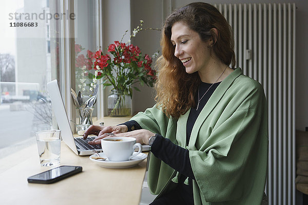Lächelnde Frau mit Laptop und Kaffee am Tisch