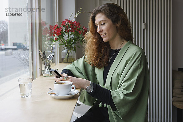 Junge Frau beim Telefonieren und Kaffeetrinken im Cafe
