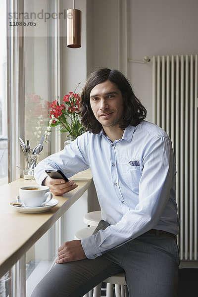 Porträt eines Mannes mit Smartphone beim Kaffeetrinken im Cafe