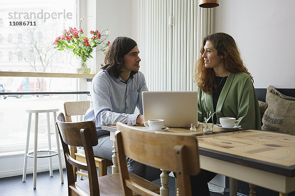 Freunde diskutieren bei der Benutzung des Laptops im Cafe