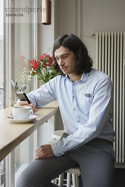 Mann mit Smartphone beim Kaffeetrinken im Cafe