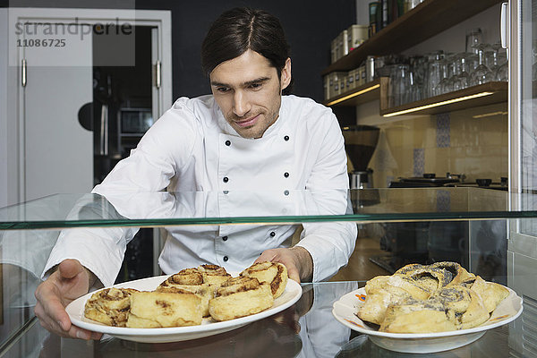 Männlicher Koch mit Zimtbrötchen für den Einzelhandel im Café