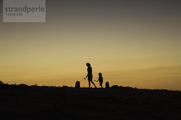 Silhouette Frau und Junge  die bei Sonnenuntergang auf dem Feld gegen den klaren Himmel laufen.